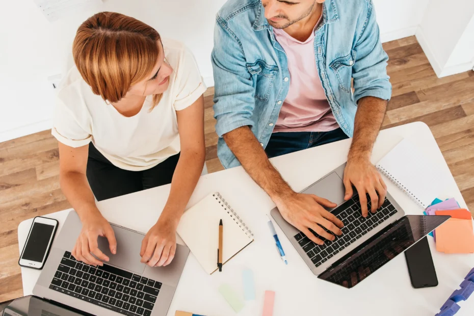 Sonrientes, hombres y mujeres, sentados en el lugar de trabajo, usando computadoras portátiles y mirándose entre sí